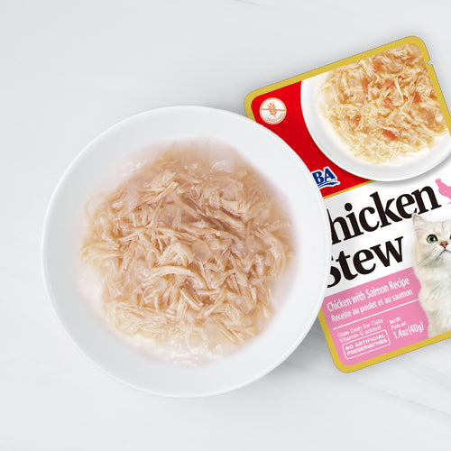 Cat food package of chicken stew with salmon recipe next to a bowl of the product on a white background