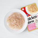 Cat food package of chicken stew with salmon recipe next to a bowl of the product on a white background