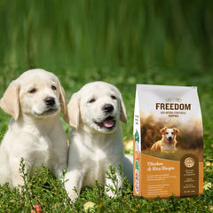 Two puppies sitting in grass with a bag of Freedom Puppy food.